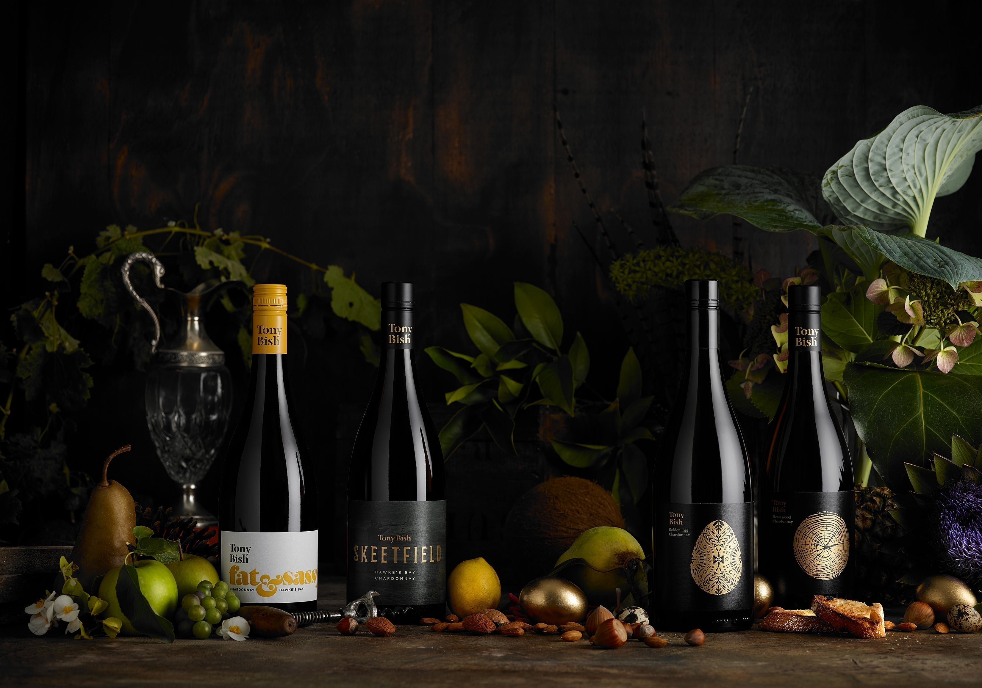 Tony Bish Chardonnay bottles arranged with fruit and botanicals in a dramatic dark flatlay
