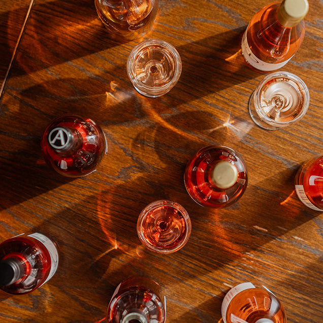 Overhead flat-lay of rosé wine bottles and glasses on a warm wooden table — a beautiful spread from Ginny's Mystery Rosé Case