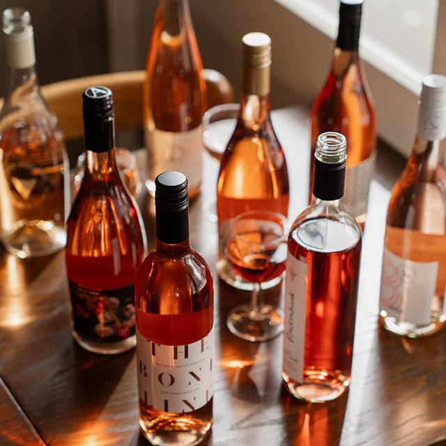 A curated selection of rosé wine bottles arranged on a dark wooden table — the inspiration behind Ginny's Mystery Rosé Case.